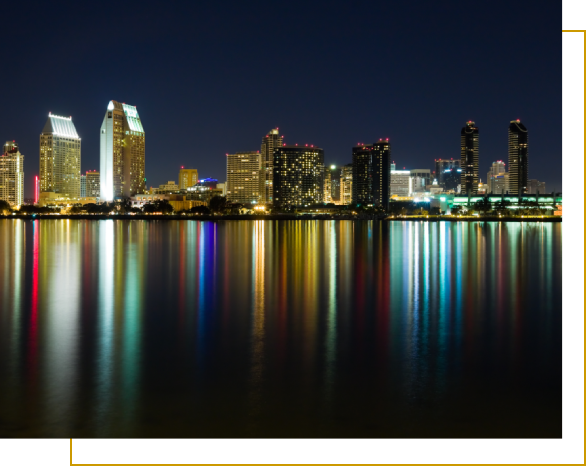 A city skyline at night with water in the foreground.